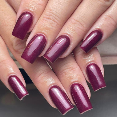 Close-up of a hand with dark purple nail polish on a neutral background