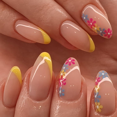 Nails with floral designs and yellow tips on a hand