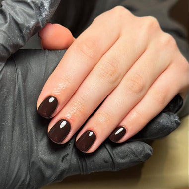Hand with dark nail polish being held by a gloved nail tech hand
