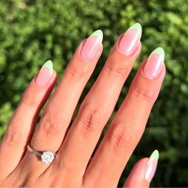 Hand with light pink and green nails wearing a silver ring against a blurred green background