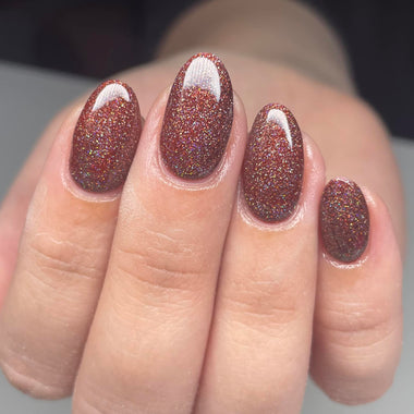 Close-up of a hand with glittery brown nail polish on a neutral background