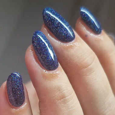 Close-up of a hand with blue glittery nail polish on a neutral background