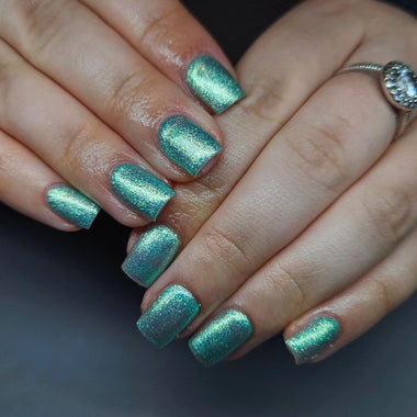 Close-up of hands with teal glittery nail polish on a dark background