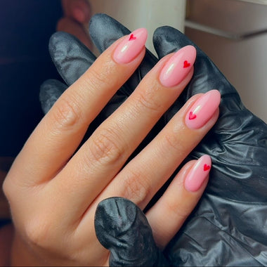 Hand with pink nails and heart designs wearing black gloves.