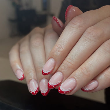 Close-up of hands with red and white nail design on a blurred indoor background