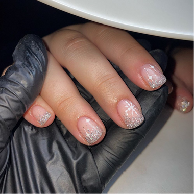 Hand with glittery nail polish being manicured by a gloved hand.