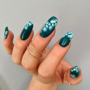 Hand with teal nail polish featuring a marble pattern on a gray background