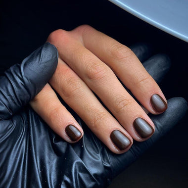 Hand with brown nail polish wearing a black glove against a dark background