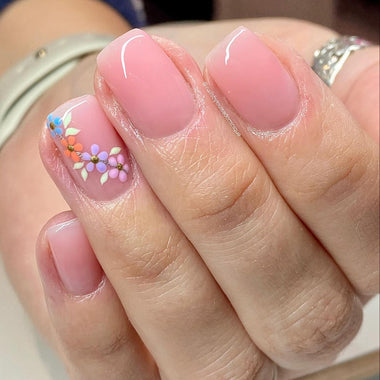 Close-up of a hand with pink nails featuring floral designs.