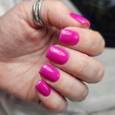 Hand with bright pink nails and a ring on a neutral background