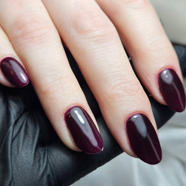Close-up of hands with dark purple nail polish on a neutral background
