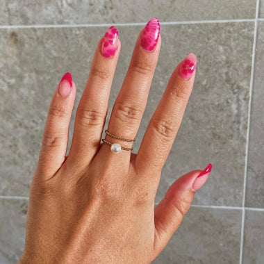 Hand with pink nail polish and a gold ring on a tiled background