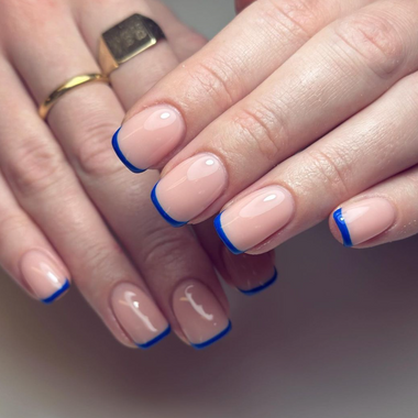 Close-up of hands with nails having a blue tip design on a neutral background