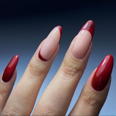 Close-up of a hand with red and nude nail polish against a blue background