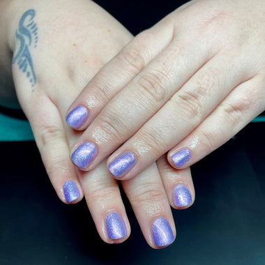 Close-up of hands with purple glittery nail polish on a dark background