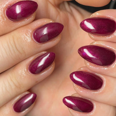 Close-up of hands with burgundy nail polish on a neutral background