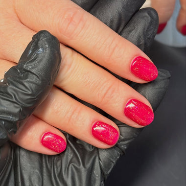 Hand with pink glittery nails wearing black gloves on a neutral background