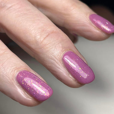 Close-up of a hand with pink glittery nail polish on a neutral background