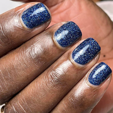 Hand with blue glittery nail polish on a blurred background