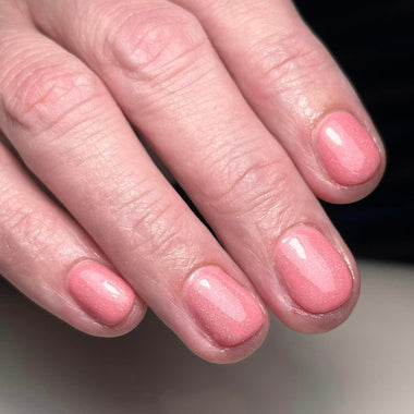 A close-up of a hand with neatly manicured nails painted in a glossy dusty pink color.