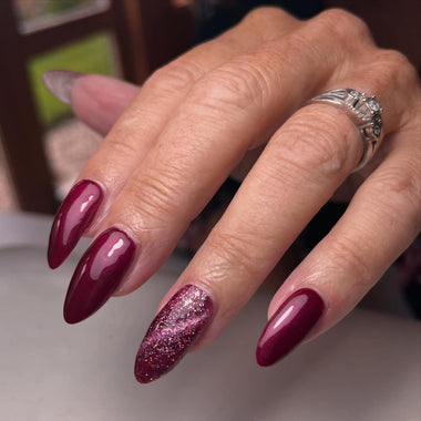 Close-up of a hand with burgundy and glittery nails wearing a ring.