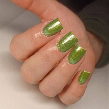 Hand with green glittery nail polish on a neutral background