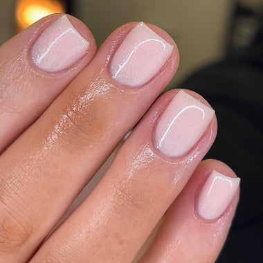 Close-up of a hand with light pink nail polish on a blurred background