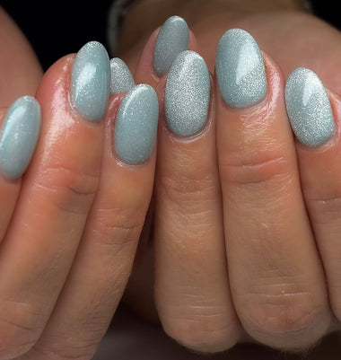 Close-up of a hand with light blue glittery nail polish on a neutral background