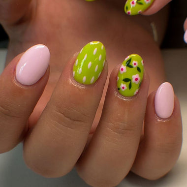 Close-up of a hand with green and pink nail art on a neutral background