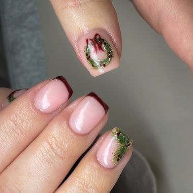 Close-up of a hand with decorative nail art featuring green and red designs.