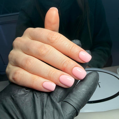 Hand with pink nail polish wearing a black glove against a blurred background