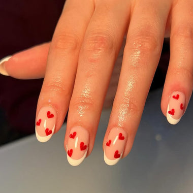 Hand with red heart nail design on a neutral background