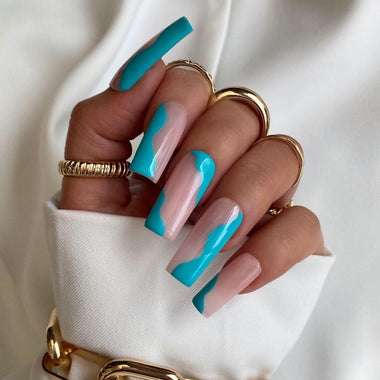 Hand with turquoise and pink nail design wearing gold rings on a white background