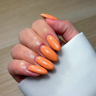 Hand with orange nail polish on a light wooden surface