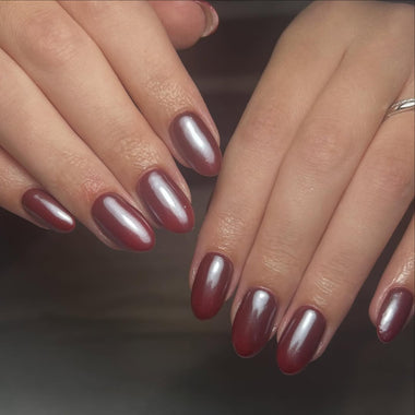 Close-up of hands with burgundy nail polish on a dark background