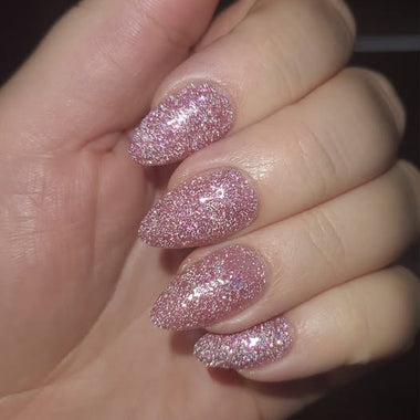 Hand with pink glittery nails against a dark background