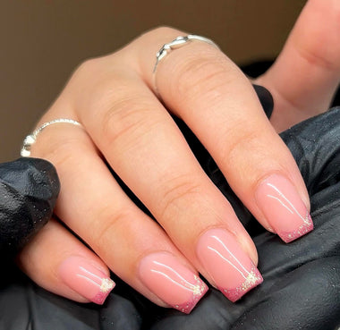 Close-up of a hand with pink nails and glittery accents, wearing a black glove.