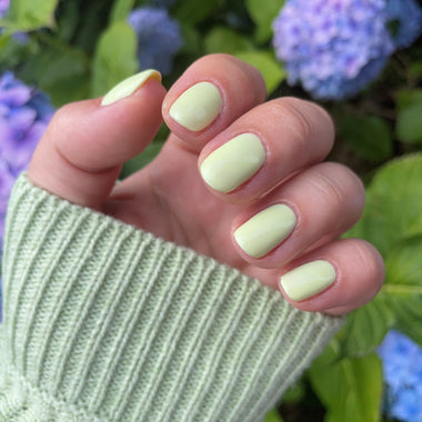 Hand with light green nail polish against a background of purple flowers
