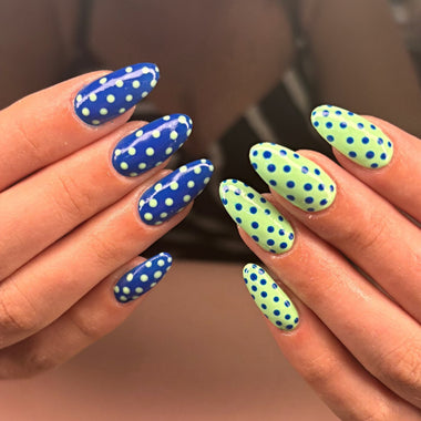Nails with blue and green polka dot design held by a person.