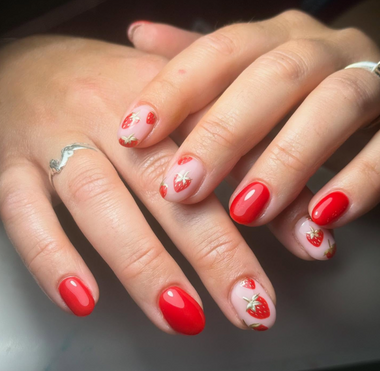 Close-up of hands with red nail polish and strawberry designs on a neutral background