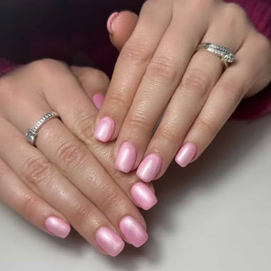Close-up of hands with pink nail polish and rings on a neutral background