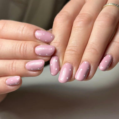 Close-up of hands with pink nails with white polka dots on a neutral background