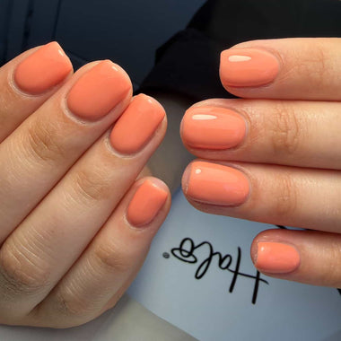 Close-up of hands with peach-colored nail polish against a blurred background