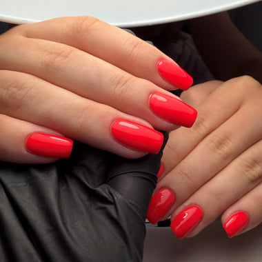 Close-up of hands with bright red nail polish on a neutral background