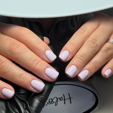 Close-up of hands with light purple nail polish in front of a 'Helis' product.