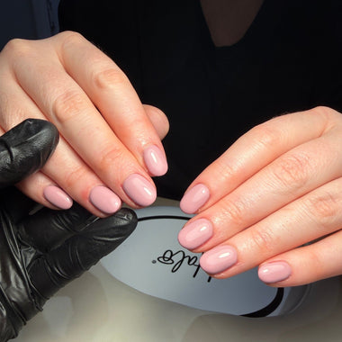 Close-up of hands with pink nail polish applying a product to a white container with 'Kiehl's' branding.