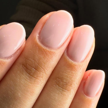 Close-up of a hand with light pink nail polish on a dark background