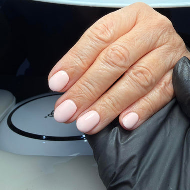 Hand with light pink nail polish wearing a black glove against a blurred background