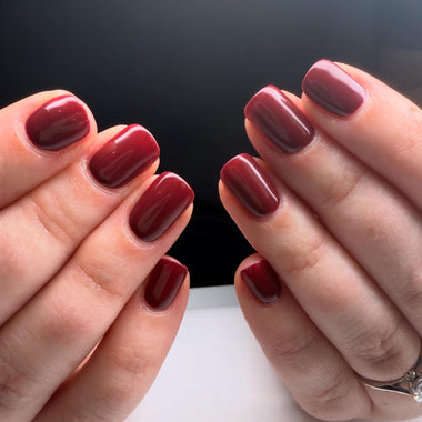 Close-up of two hands with burgundy nail polish on a black background