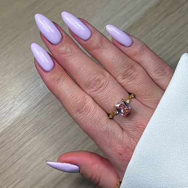 Hand with lavender nail polish and a pink gemstone ring on a light wooden surface